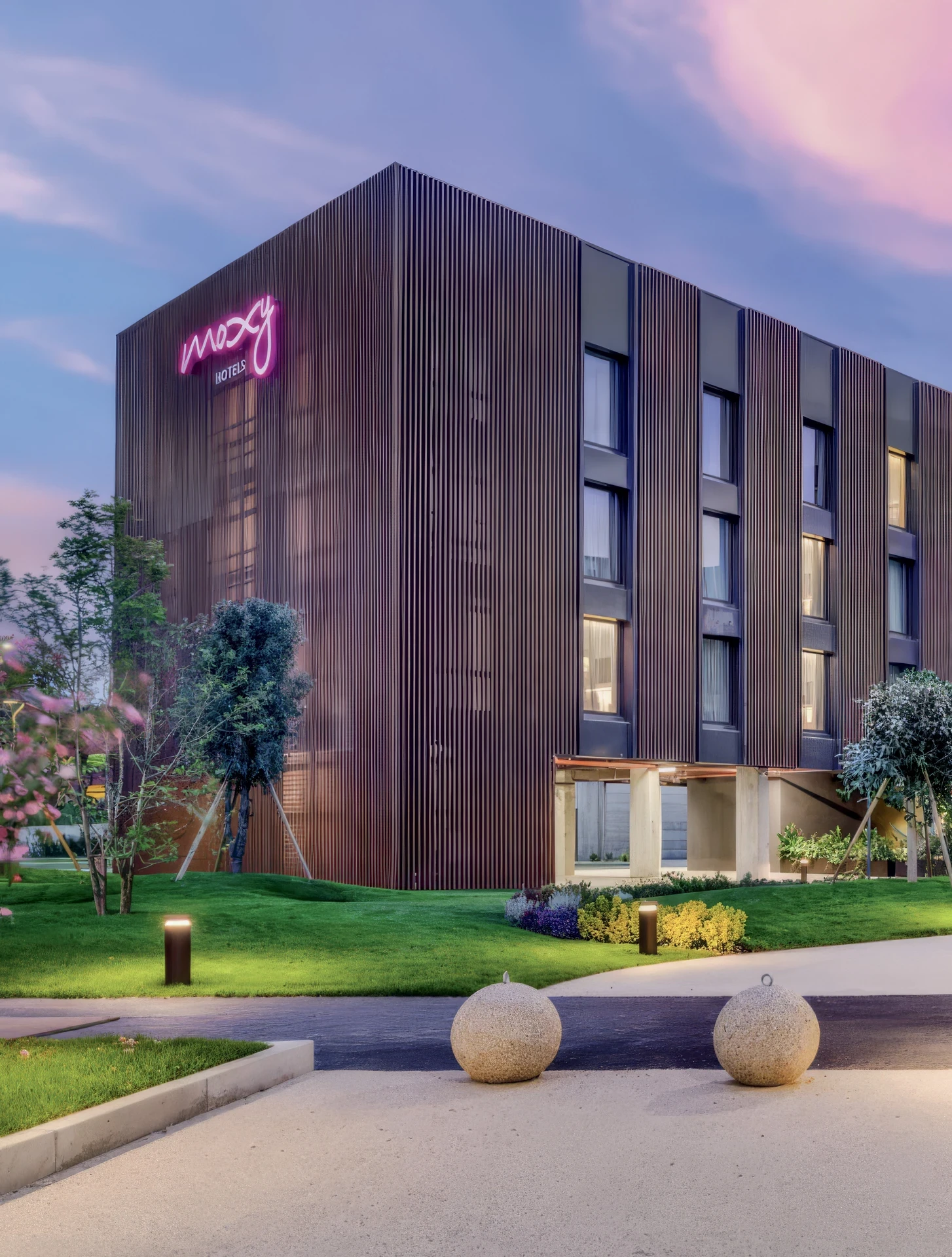 Facciata esterna del Moxy Hotel by Marriott con insegna al neon al tramonto. Torre Annunziata, Napoli. Arredamento su misura Tomasella Contract, 2024.